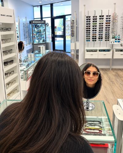 Customer trying on sunglasses in the mirror at Eyeglass Gallery